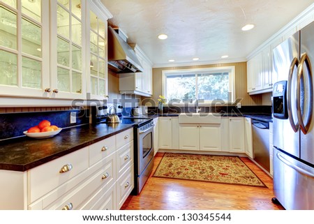 White kitchen interior with large sink, window, hardwood floor.