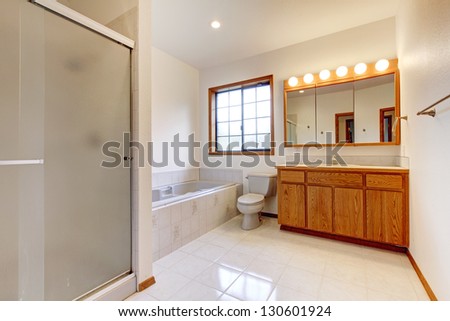 Large white bathroom with tub, shower, shiny tiles and wood cabinet.