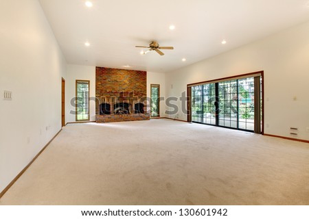 Very large empty living room with brick fireplace and sliding doors to the back yard.
