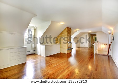 Large long attic room with fireplace. Empty with golden hardwood.