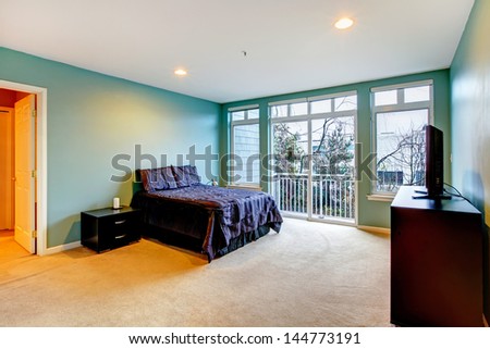 Large bright blue bedroom with purple bed and balcony door.