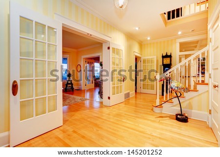 Golden bright yellow luxury home main hallway, entrance with staircase and open doors to living room.