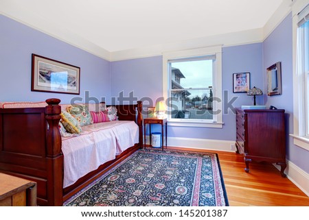 Purple guest bedroom with single wood day bed and blue rug.