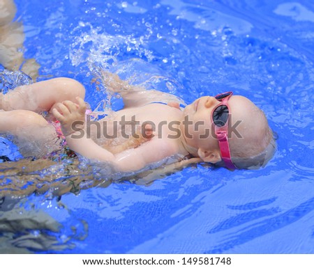 Small baby girl is swimming in the pool. She is three months old.