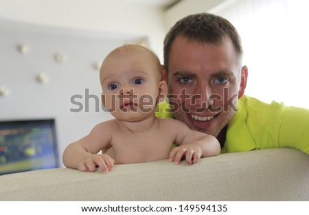 Little baby and young father are watching sport on TV in modern apartment. Baby is three months old.