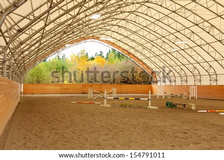 Covered open horse arena with sand and white ceiling.