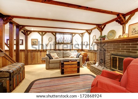 Rustic Furnished Family Room With A Stoned Background Fireplace, Old Couch, Country Style Rug And Ceiling Beams Design