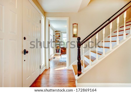 Bright hallway with wooden light brown stairs and whiskey color hardwood floor