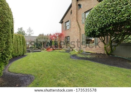Backyard of stoned classic house with green trim , red tree and hedge