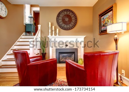 Classic designed family room with comfortable red chairs, light tones fireplace, hardwood floor and beige walls