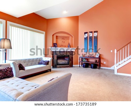 Orange Cozy Living Room With Carpet Floor, White Wood Stairs, Grey Furniture And Fireplace. Decorated Table With Candles And Wood Wall Handmade Art
