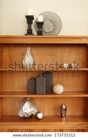Light brown wood shelf decorated with silver vases and ball, abstract metal art and candles