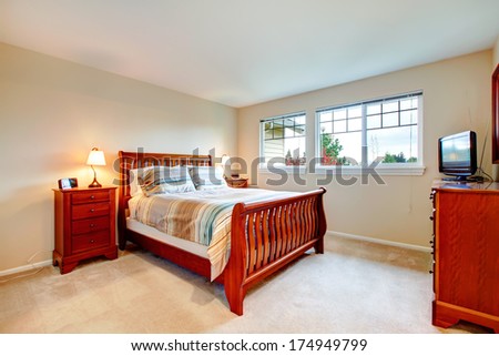 Beautiful bedroom with  light tones wall and carpet floor naturally matching brown wood bedroom furniture.