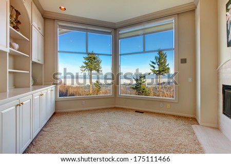 Empty bright room with beige carpet floor, angled glass wall and wood storage combination