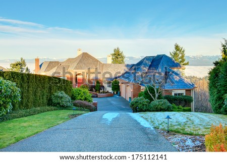 Luxury brick house with drive way and trimmed hedges. Amazing background. Winter, snowy mountains view