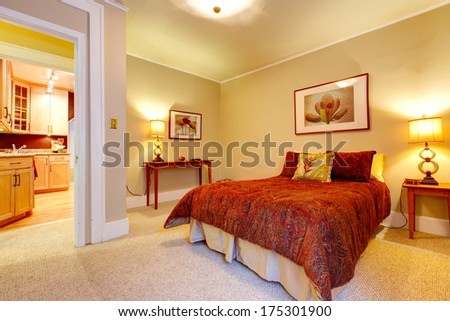 Bright bedroom with beige carpet floor and yellow walls. Red bedding, red frame wall picture and tables accomplish  design