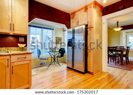 Cozy kitchen with burgundy walls and light wood cabinets. Open to bright dining area