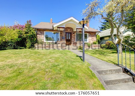 One story stoned house with wrought iron column porch and green lawn