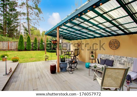 Wood patio pergola with iron table set, sofa and chairs overlooking beautiful green lawn and fir trees. Patio area decorated with iron arts and flower pots.