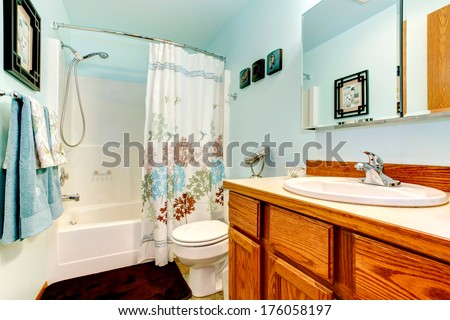 Light blue bathroom with wood cabinets. tile floor. Decorated with blue and white towels and curtains