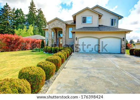 Big siding house with garage and high column porch. Green lawn with trimmed hedges and red bushes make the curb appeal stand out