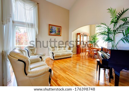 Luxury living room with high vaulted ceiling and hardwood floor, leather couch, loveseat, piano.