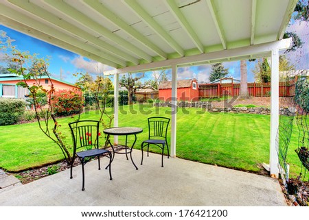 Attached pergola with patio table set overlooking beautiful green lawn, trees and red wooden shed