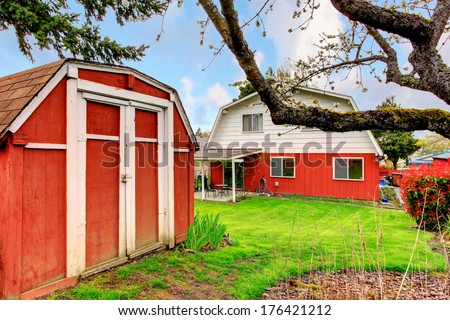 Backyard with patio area, green lawn and flourishing bushes, red wooden shed