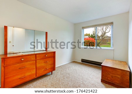 Bright small room with window. Room with beige carpet floor furnished with antique wooden chest and cabinet with mirror