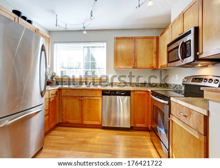 Bright kitchen room with wood cabinets, steel modern appliances, hardwood floor and decorated back splash