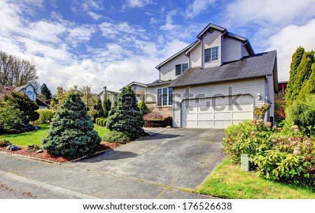 Siding house with garage. Green lawn with trimmed hedges, flourishing bushes and fir trees.