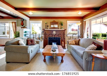 Big living room with grey carpet floor, ceiling beams, stoned background fireplace. Room furnished with sofa and loveseat, rustic coffee table.  Decorated with vase and dry branches.