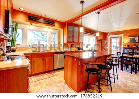 Big Kitchen With Window And Beige Concrete Floor. Bright Wooden Storage Combination Matches Perfectly With Steel Appliances And Black Counter Stools. Room Extended To Dining Area