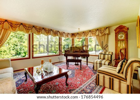Bright living room with old fashioned couch and chairs, wooden coffee table, grand piano and antique oak grandfather clock