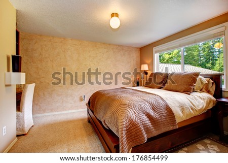 Beige bedroom with soft carpet floor. Furnished with wooden queen size bed, desk and chair