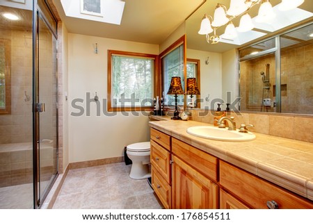 Bright bathroom with mocha tile floor, wood storage cabinet and washbasin cabinet, glass door shower