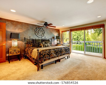 Big bedroom with walkout deck. Room furnished with antique iron frame bed, inlaid nightstand and decorated with iron wall art