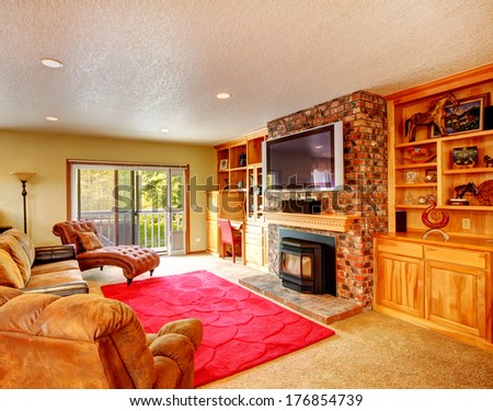 Comfortable living room with storage combination and brick wall together with fireplace and tv. Room furnished with antique armless leather chair, couch and loveseat,