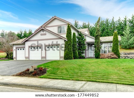 Two story clapboard siding house with garage, drive way, green lawn and fir trees
