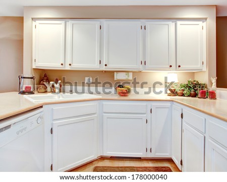 Bright kitchen with white wooden cabinets and beige counter tops.
