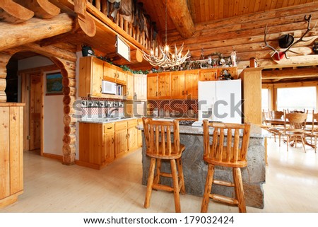 Bright kitchen room with rocky counter cabinet, rustic counter stools, horn chandelier. Log cabin house interior