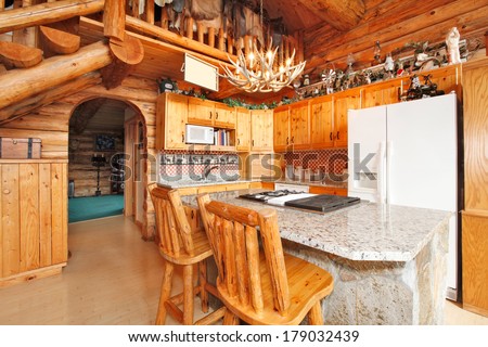 Bright kitchen room with rocky counter cabinet, rustic counter stools, horn chandelier. Log cabin house interior