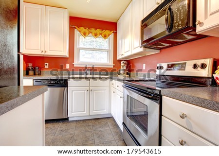 Small kitchen room with concrete tile floor, red walls, steel appliances and white wooden cabinets