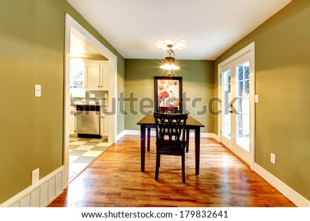 Small dining room with a hardwood floor and olive walls. Furnished with a black dining table set. View of the kitchen.