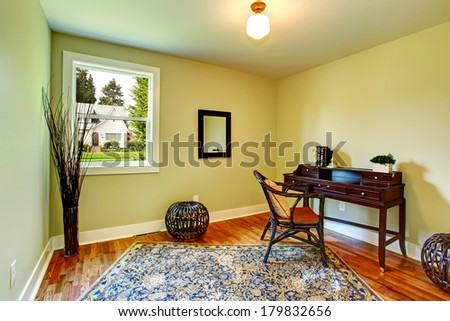Bright one window small room with olive walls and hardwood floor. Decorated with an antique chest with chair, dry branches