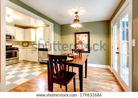 Small dining room with a hardwood floor and olive walls. Furnished with a black dining table set. View of the kitchen.