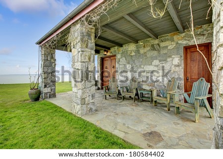Beautiful open stone porch with columns, old wooden chairs and castle style entrance door. Porch overlooking picturesque landscape.