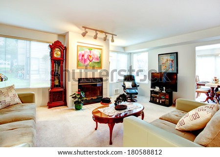 Bright living room with beige and olive sofa, love seat, antique grandfather clock and coffee table, modern leather rest chair and tv.
