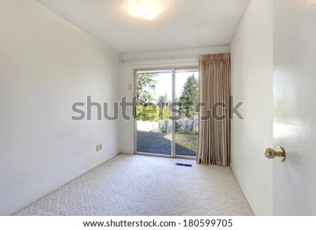 Empty white room with a beige carpet floor and beige curtains. View of the slide doors and walkout deck