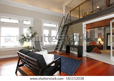 Modern living room with brick painted wall, hardwood floor and iron steep stairs. View of bedroom